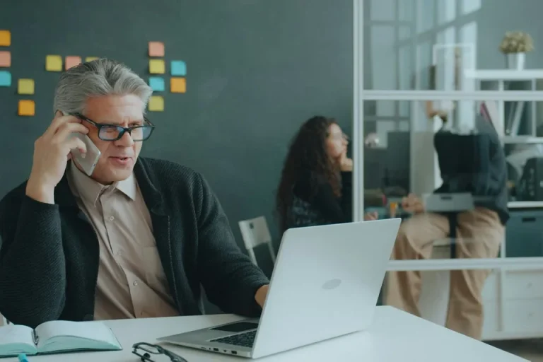 Irodai munkatárs telefonál, előtte nyitott laptop