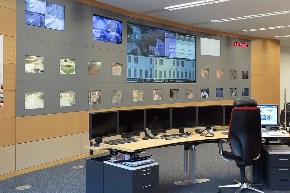 Felügyeleti központ monitorfala kameraképekkel, előtte üres operátori pult több képernyővel